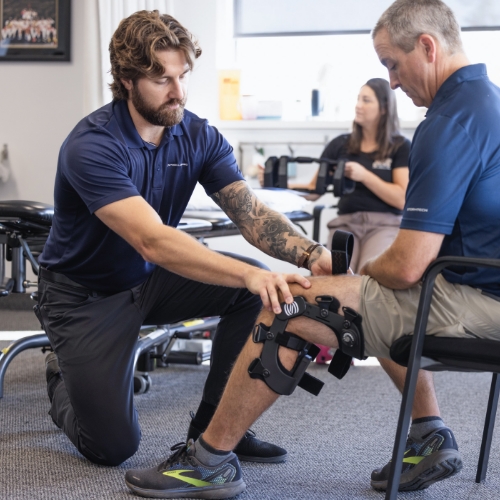 A male clinician is sizing a patient for a custom knee brace. He is currently positioning the brace for proper alignment on the patient.