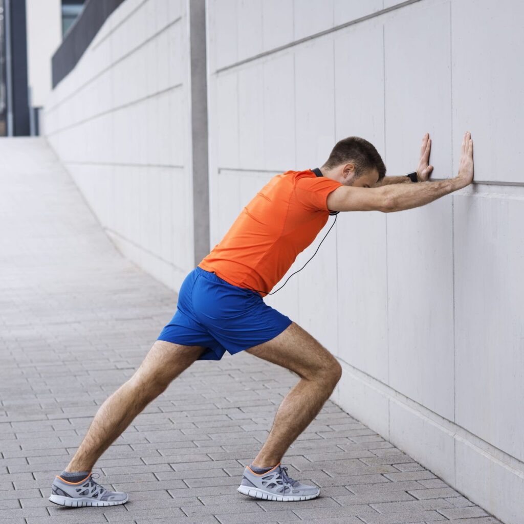 Runner leaning against a wall to stretch out their calves during their warm-up.