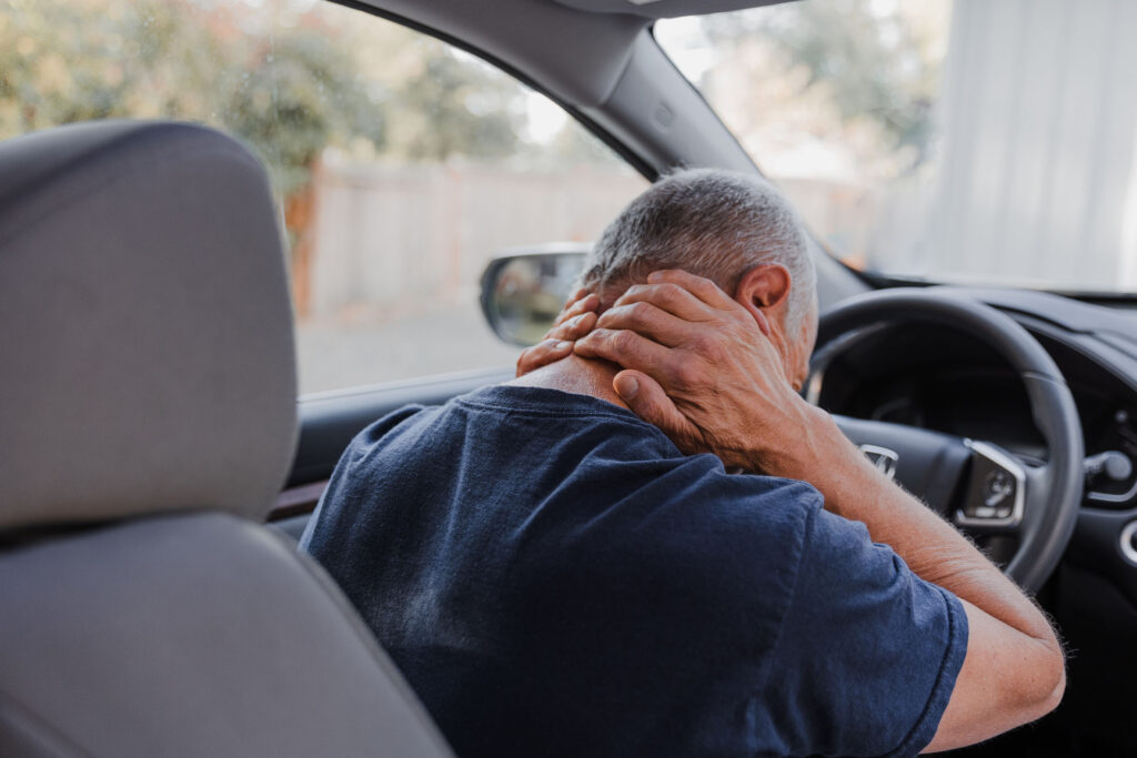 Image of person holding neck sitting in car from whiplash